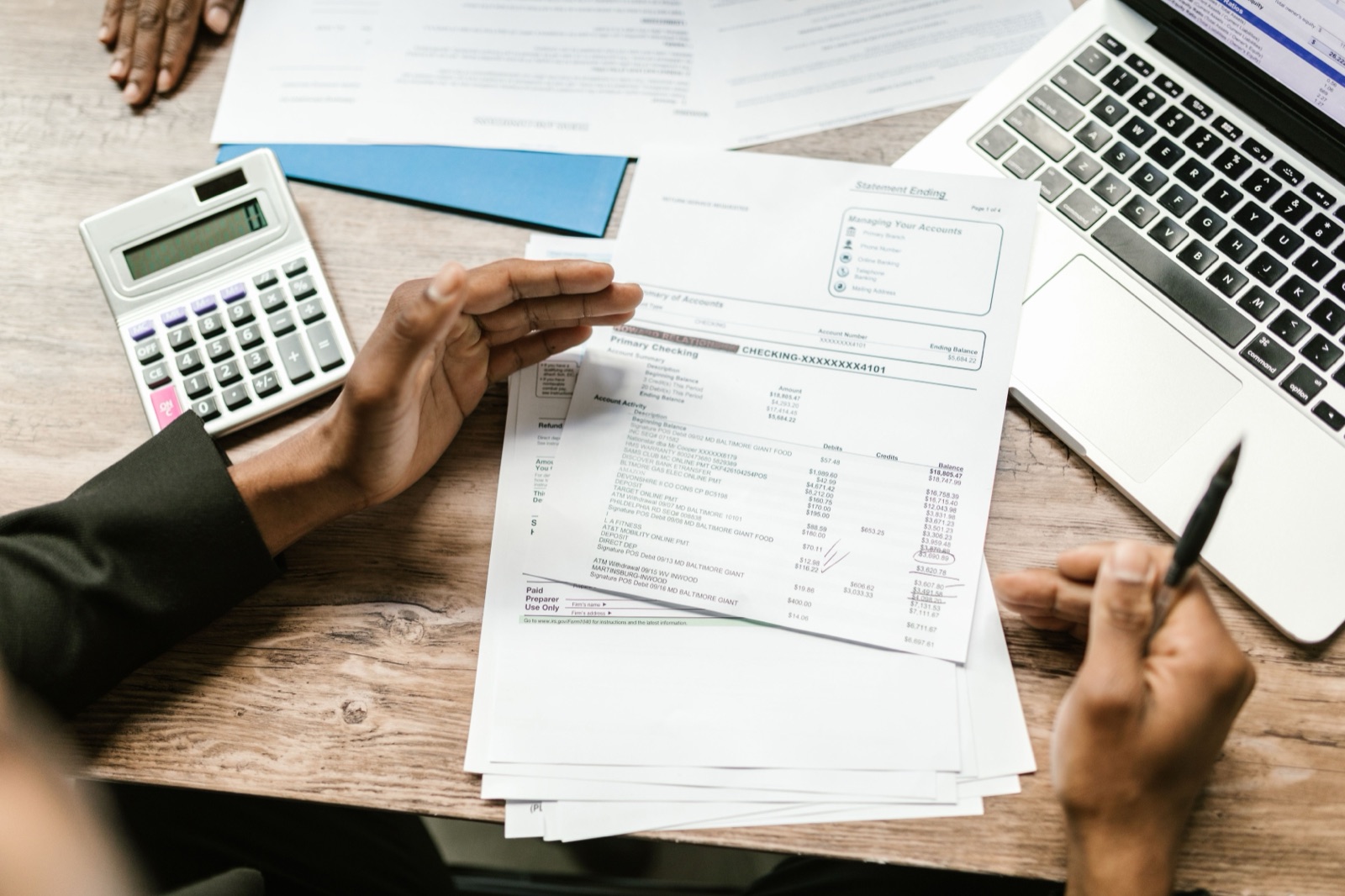Bank statement, calculator, laptop, and paperwork on a desk during a financial review.